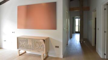 Un pasillo con un armario de madera, una obra de arte naranja grande y una puerta que da a otra habitación.