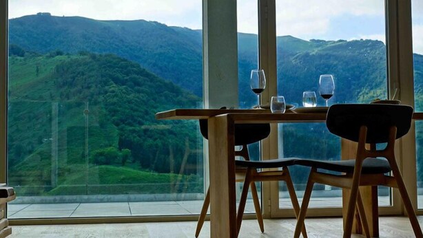 A dining table with chairs and wine glasses, set against a backdrop of a mountainous landscape through large windows. - Arantza Apartamentuak (Arantza)