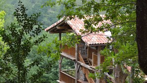 A treehouse with a red-tiled roof, wooden staircase, and a view of the surrounding forest. - Arantza Apartamentuak (Arantza)