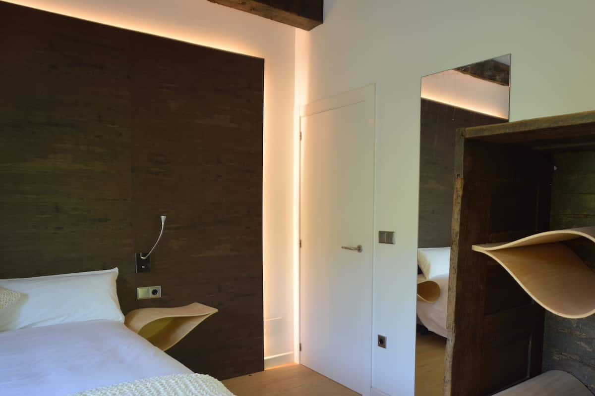 A modern bedroom with a bed, bedside table, and a mirror reflecting the room.