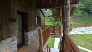 A wooden cabin with a stone wall, a wooden deck, and a view of a forested area. - Arantza Apartamentuak (Arantza)