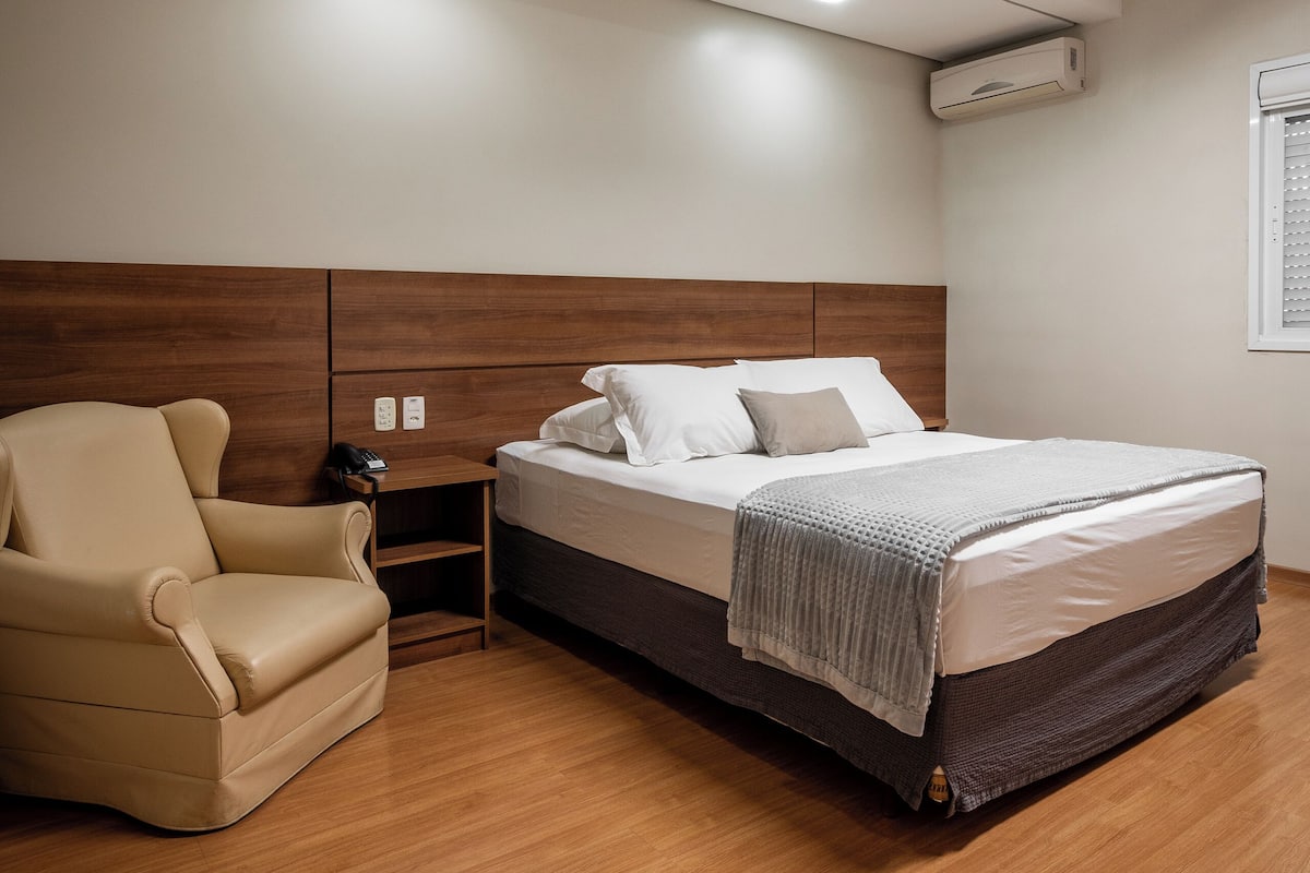 A bedroom with a bed, a chair, a bedside table, and a ceiling light.