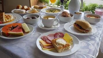 Una mesa de desayuno con diversos alimentos, como waffles, fruta, sándwiches y bebidas.