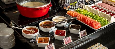 A buffet with various food items, including a red pot of soup, sliced tomatoes, and cheese.