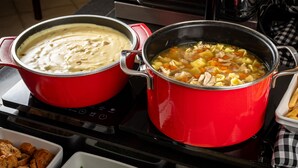 Two red pots on a stove, one with a creamy soup and the other with a vegetable soup. - Hotel Kindermann (Cacador)
