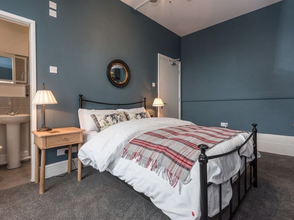 Een slaapkamer met een bed, nachtlampjes, een spiegel en een deur.