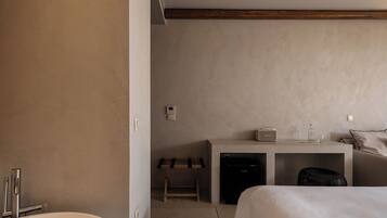 A hotel room with a bed, a desk with a computer, a small stool, a black trash bin, and a white sink.