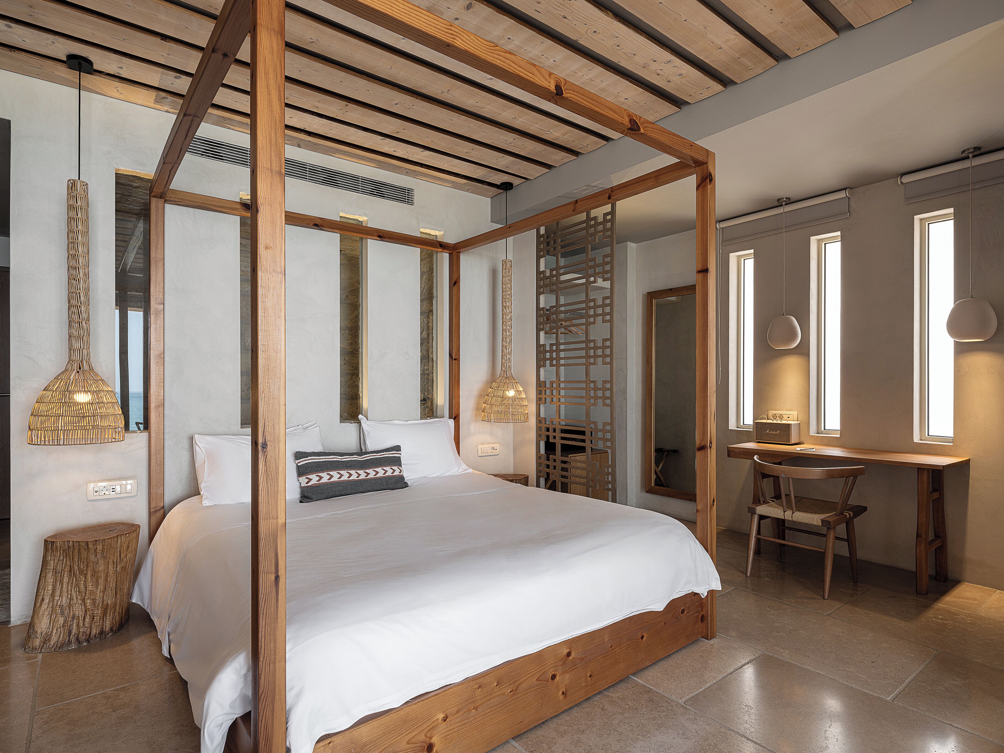 A bedroom with a four-poster bed, wooden beams, a desk, and a chair.