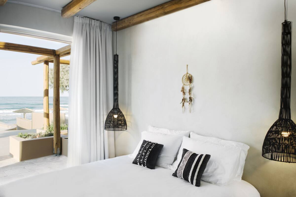 Un dormitorio con una cama grande, ropa de cama blanca y dos lámparas colgantes negras.