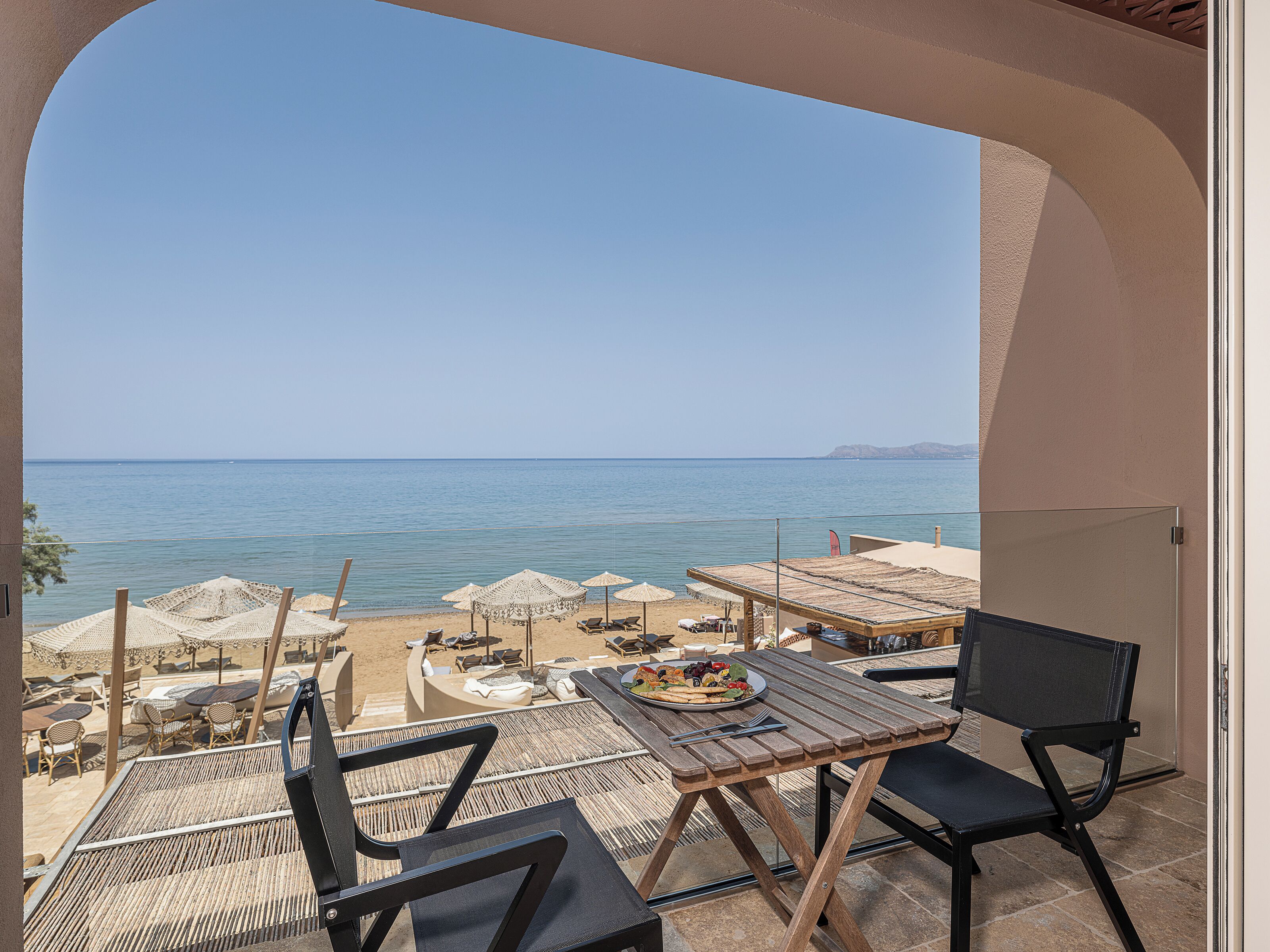 A terrace with a view of the sea, furnished with tables and chairs, and a buffet table with food.
