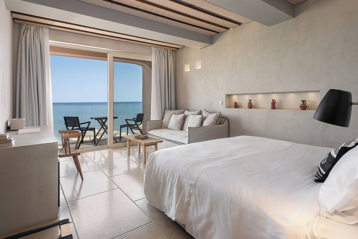 Habitación de hotel con una cama grande, un escritorio y una silla cerca de la ventana. Se ve el mar a través de la ventana.