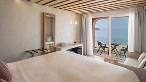 Quarto de hotel com cama, escrivaninha, cadeira e vista para o mar.
