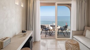 Quarto moderno com cozinha, mesa de jantar com cadeiras, sofá e vista para o mar através de grandes portas de vidro.