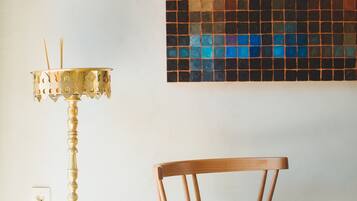 Une pièce avec une chaise en bois, un lampadaire en laiton et un mur décoré d’une mosaïque colorée.