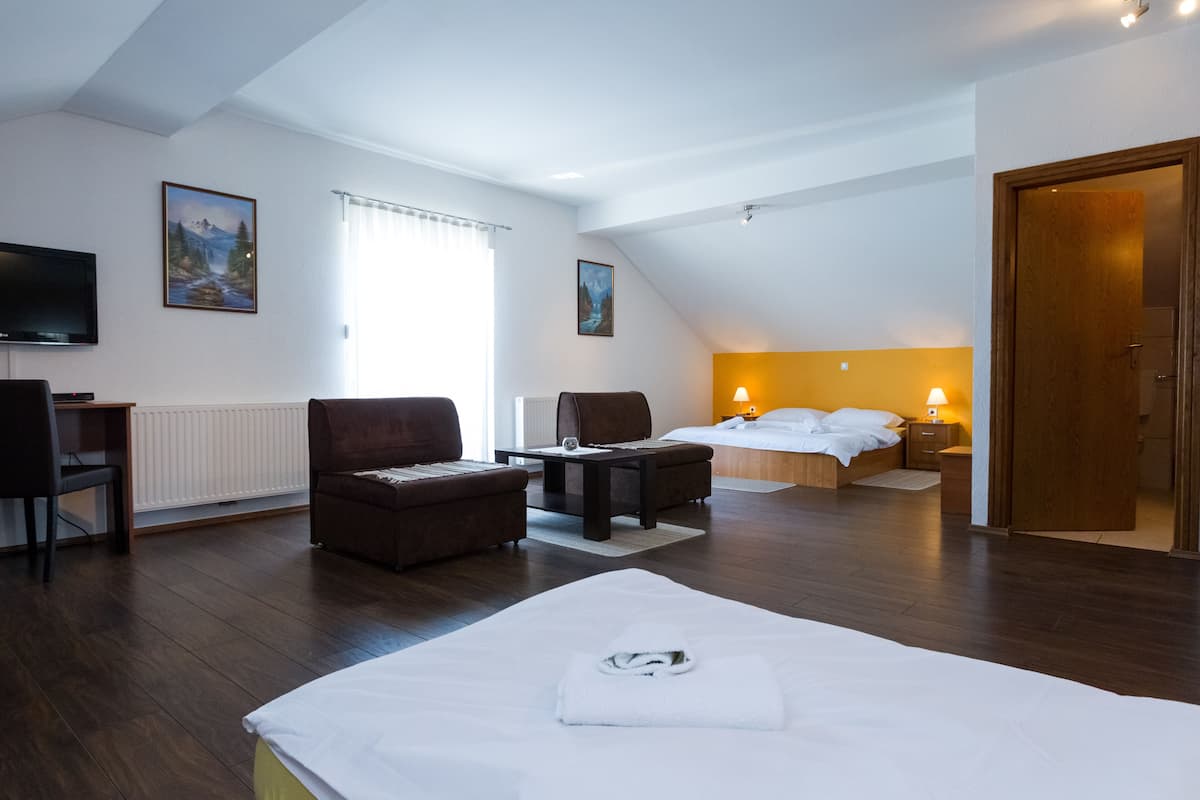 Une chambre d’hôtel comprenant un lit, deux fauteuils, une petite table, un téléviseur et des œuvres d’art accrochées aux murs.