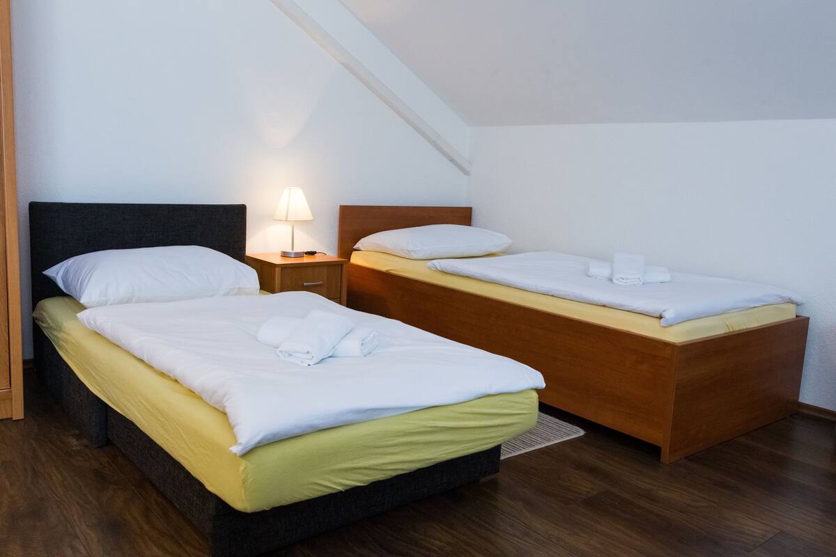 Une chambre avec deux lits, chacun doté d’une tête de lit en bois et d’une table de chevet avec une lampe.