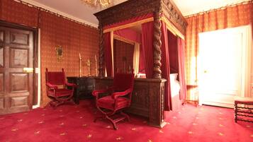 A room with a four-poster canopy bed, two red upholstered chairs, a wooden desk, and a large mirror.