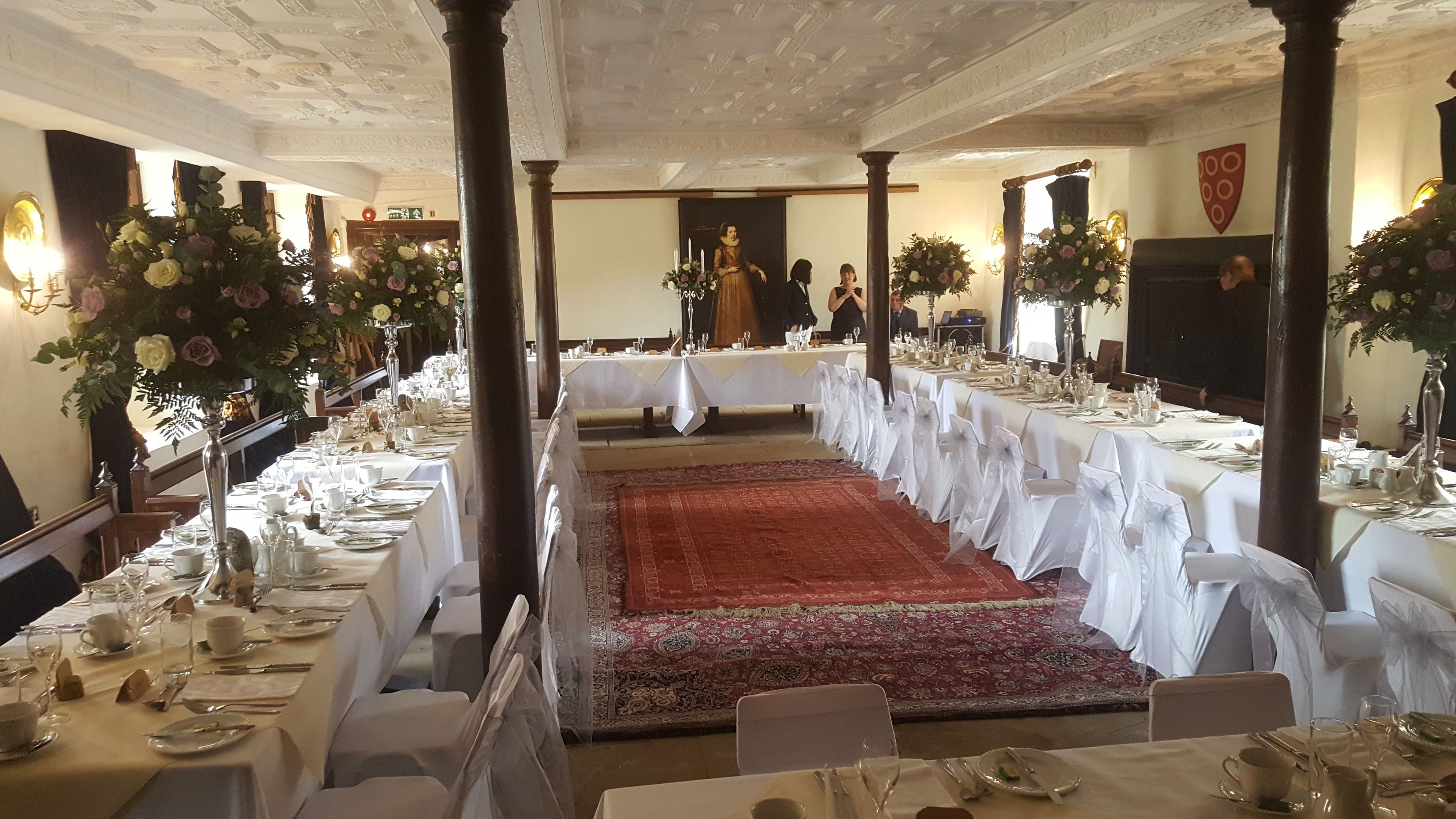 A banquet hall with long tables set for a formal event, featuring a central aisle and ornate ceiling.