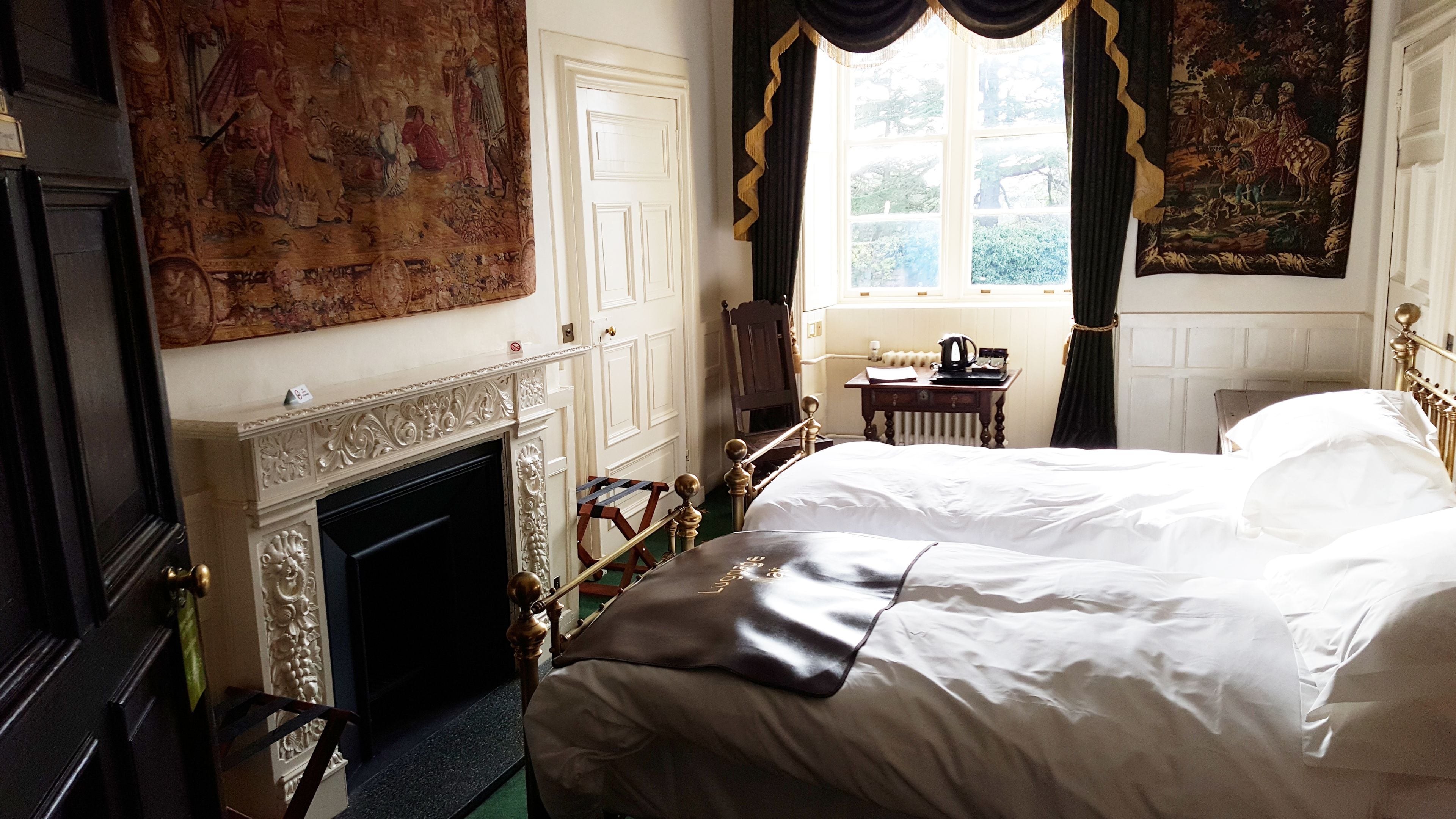 A bedroom with a large bed, a fireplace, a window with curtains, and a tapestry on the wall.