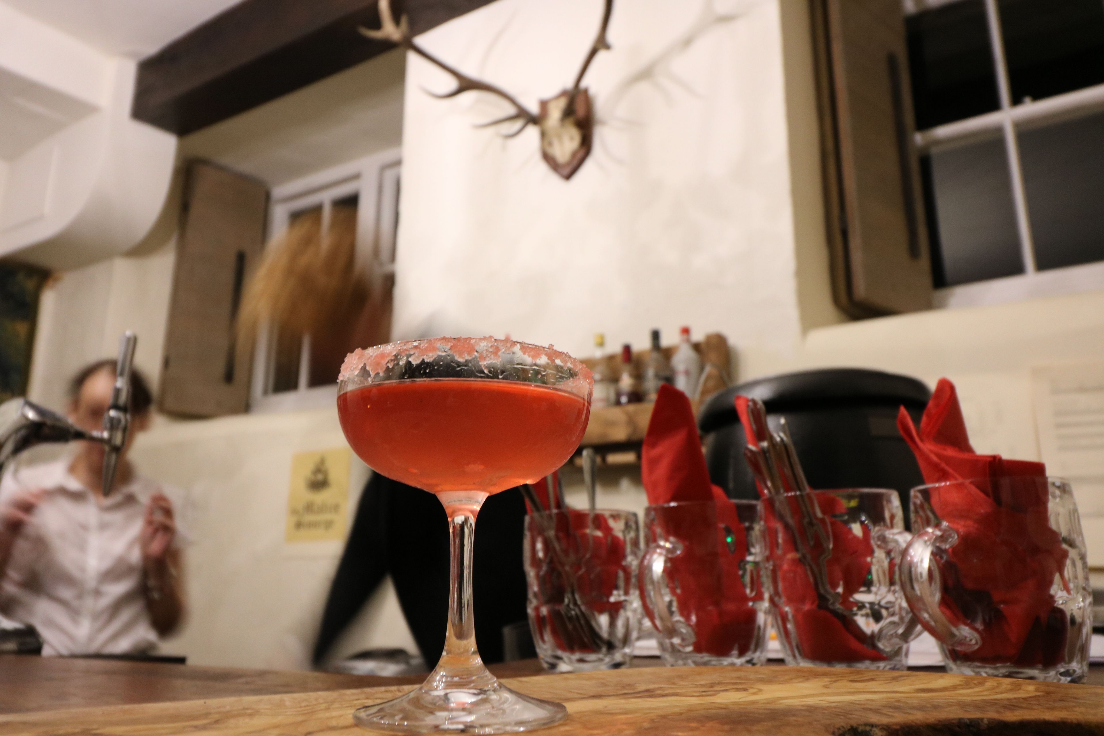 Eine Bar mit einem Cocktailglas, Gläsern und einem Hirschgeweih an der Wand.
