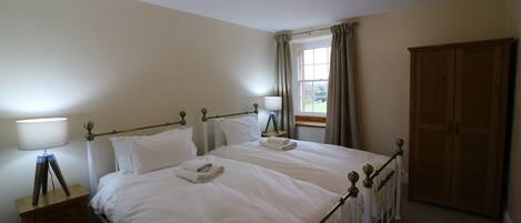 A neatly made twin bed with white linens, a bedside table with a lamp, and a wooden wardrobe.