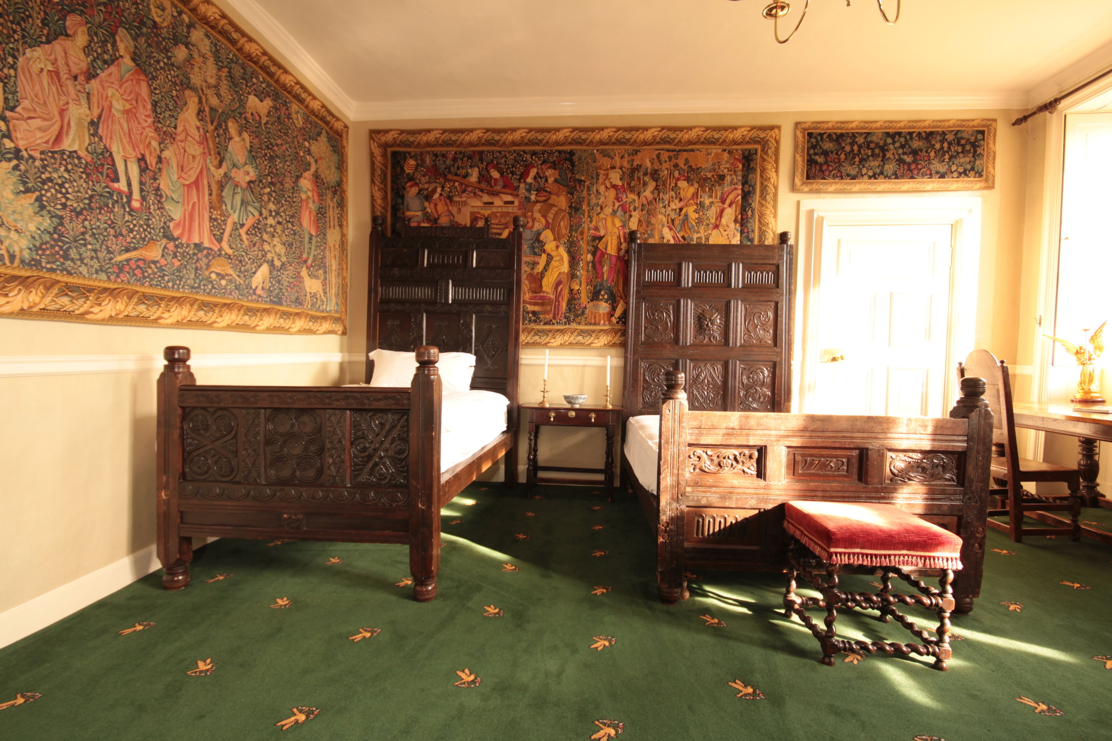 A traditional bedroom with a large tapestry, a four-poster bed, a wooden bench, and a small table.
