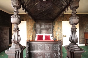 Quarto com uma cama grande e ornamentada, teto de madeira e tapete verde.