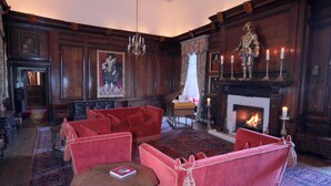 A traditional room with a fireplace, red upholstered furniture, and a chandelier. - Appleby Castle (Appleby-in-Westmorland)