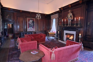Quarto tradicional com lareira, mobiliário estofado em vermelho e um candelabro.
