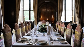 Uma sala de jantar formal com uma mesa comprida posta para refeição, ladeada por cadeiras com estofados estampados e fitas douradas.
