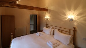 A neatly made bed with white linens and towels, a wooden headboard, and wall-mounted light fixtures. - Appleby Castle (Appleby-in-Westmorland)