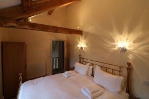Cama bem arrumada com roupa de cama e toalhas brancas, cabeceira de madeira e luminárias fixadas na parede.