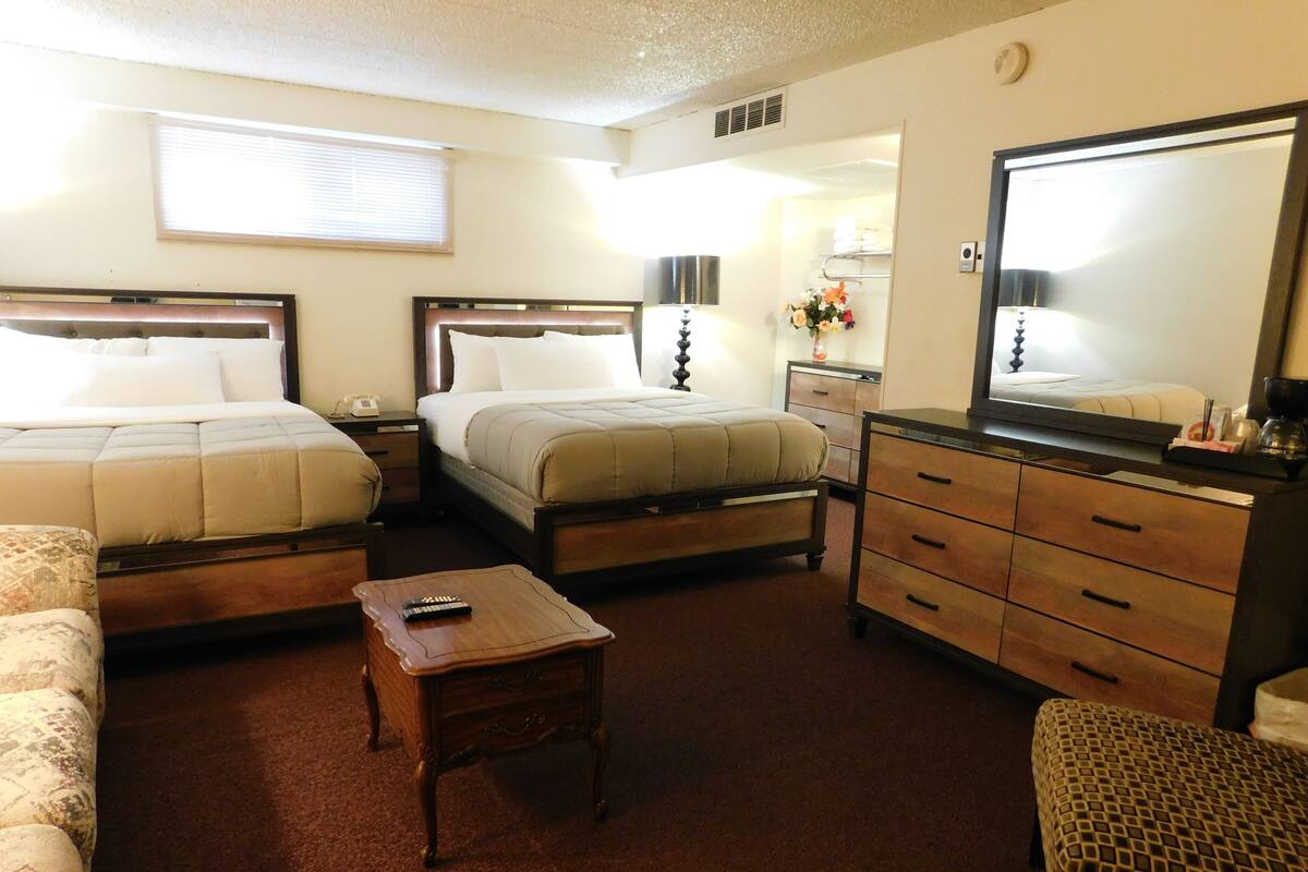 A hotel room with two beds, a wooden dresser, a small table, and a mirror.