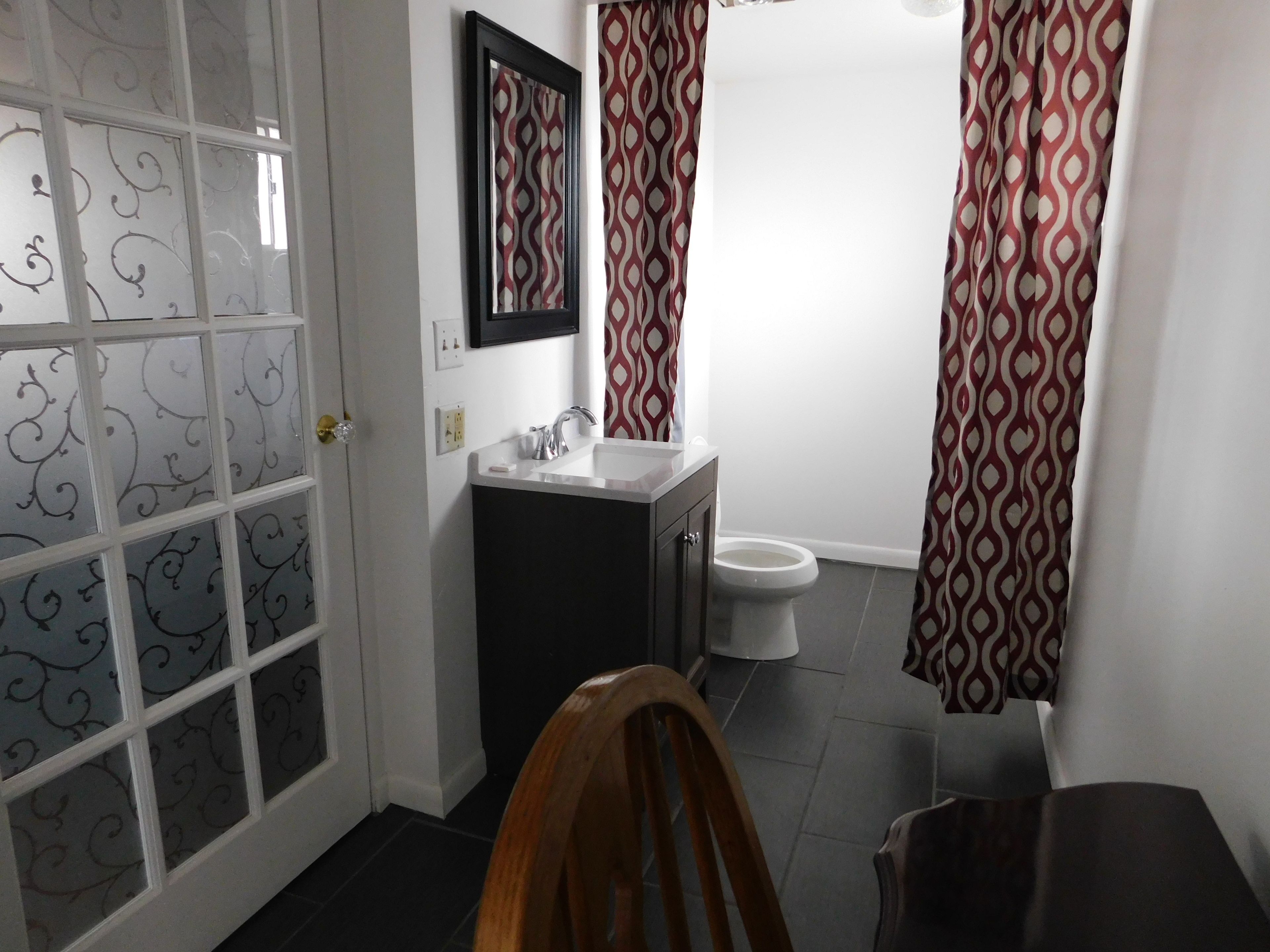 Un baño con inodoro, lavabo y espejo. Hay una cortina estampada sobre la zona de la ducha.
