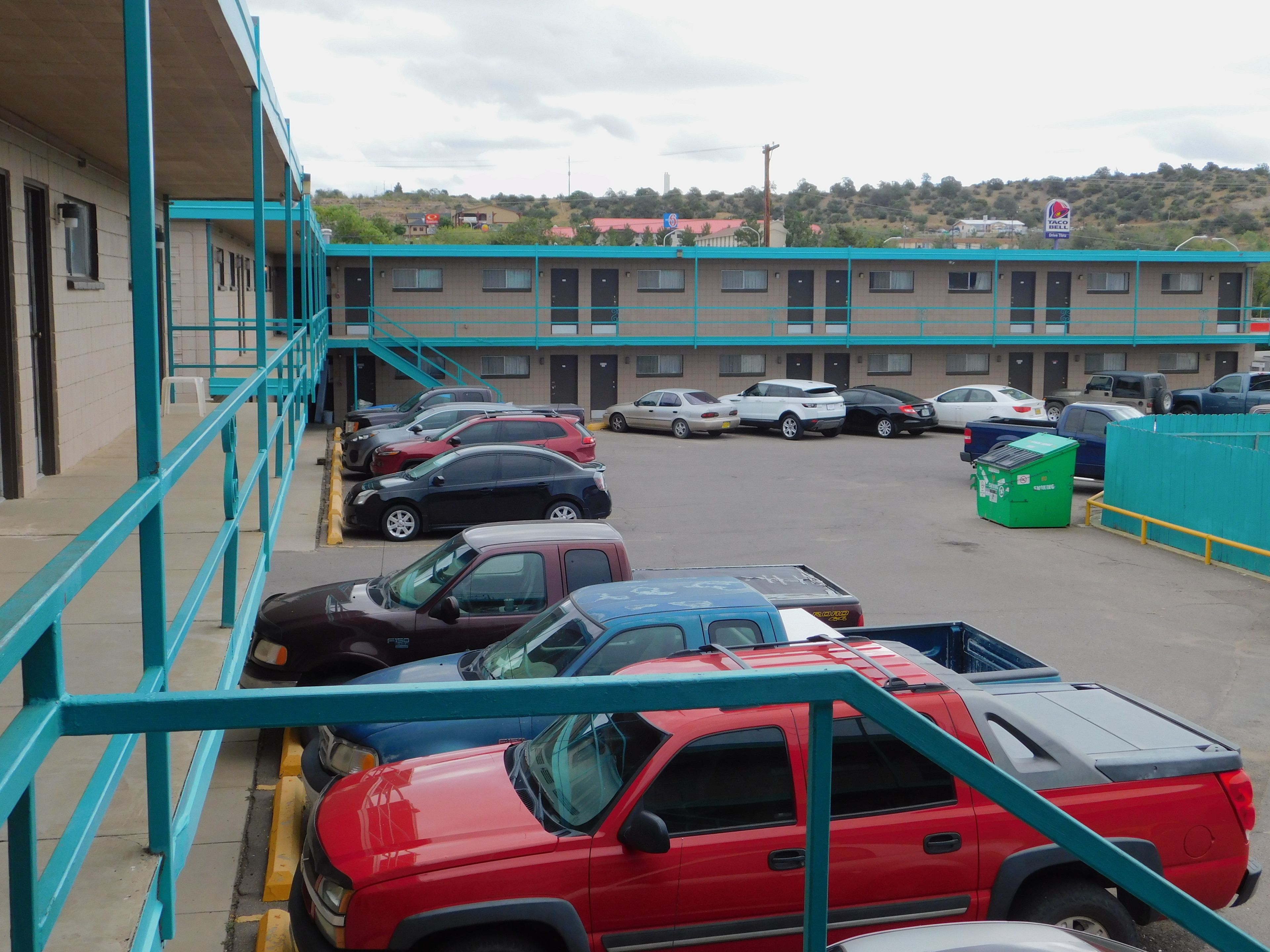 A parking lot with several cars and a building with multiple doors in the background.