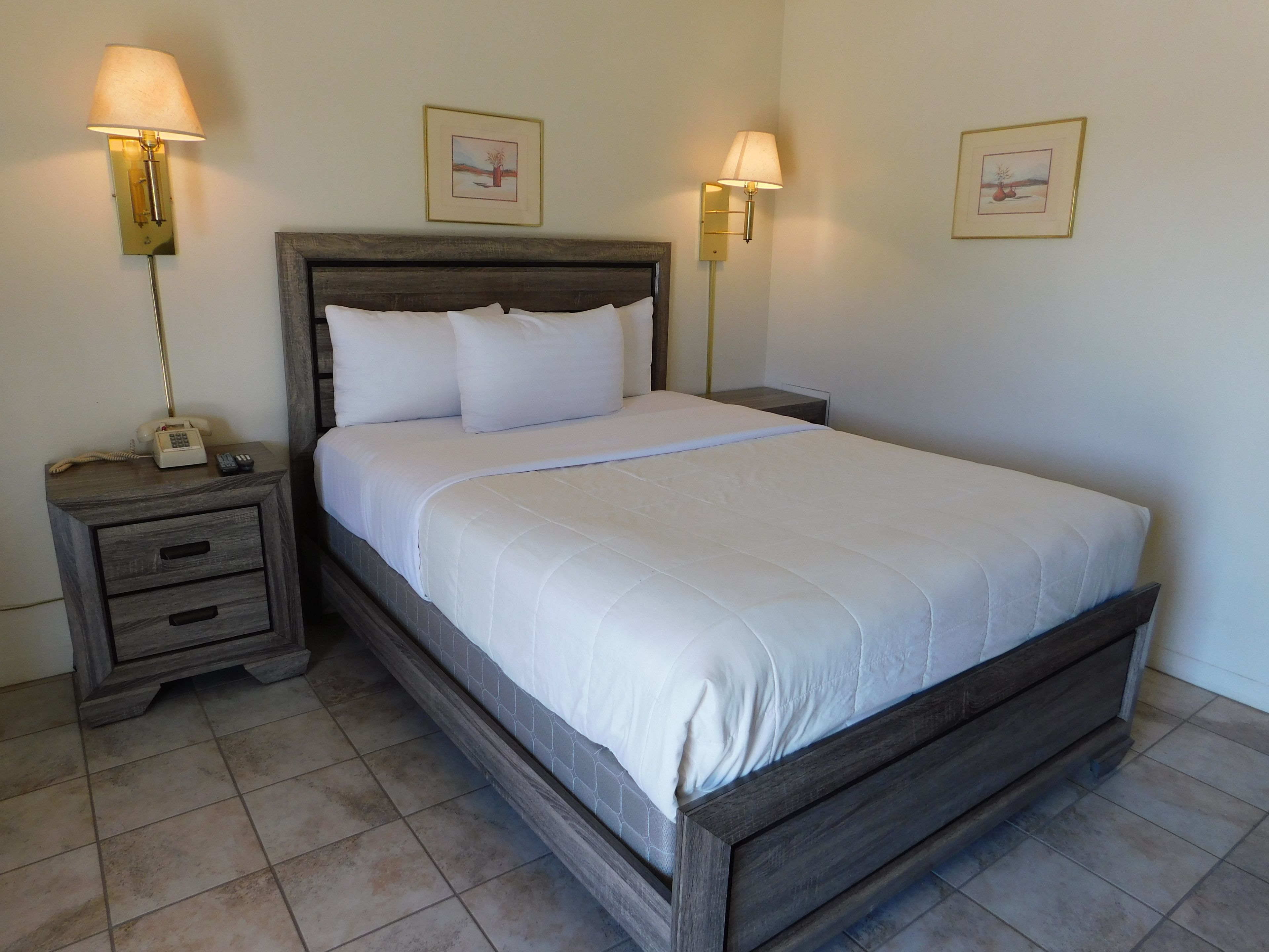Una cama bien hecha con ropa blanca, un cabecero de madera y dos lámparas de noche.