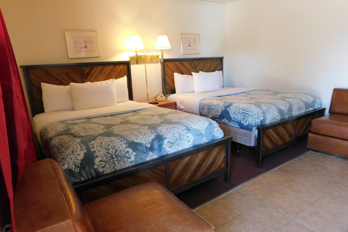 A hotel room with two beds, each with patterned bedding, a nightstand with a phone, and a brown leather chair.