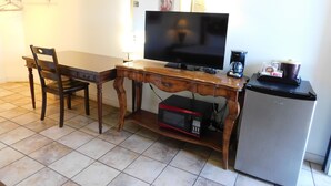 Una habitación compacta con escritorio de madera, televisión, refrigerador pequeño y una silla.