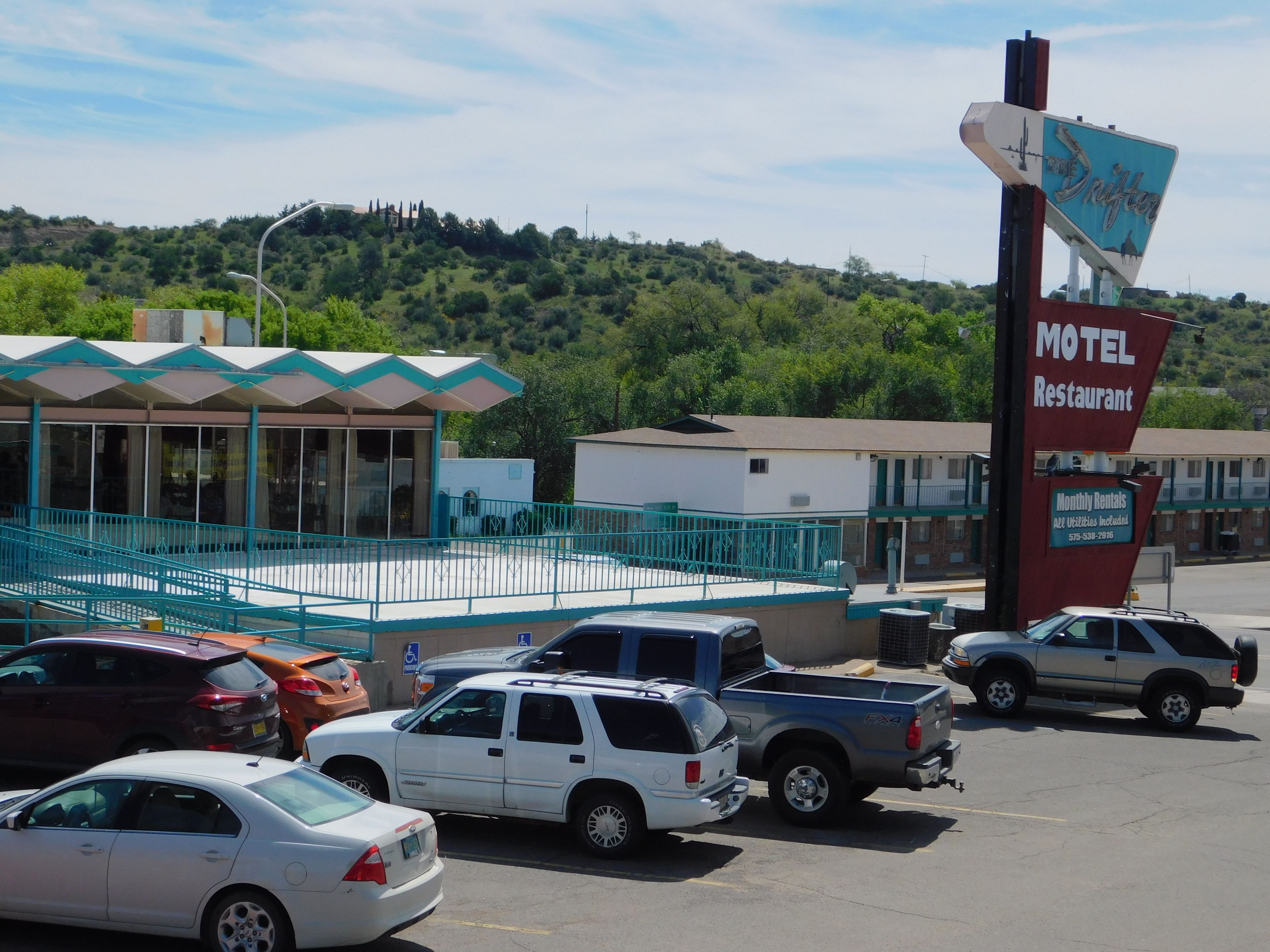A motel with a signboard, a covered outdoor seating area, and a parking lot with several cars.