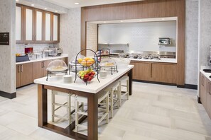 A modern kitchen with a central island, equipped with a fruit bowl and serving dishes. - Hilton Garden Inn Dallas/Arlington South (Arlington)