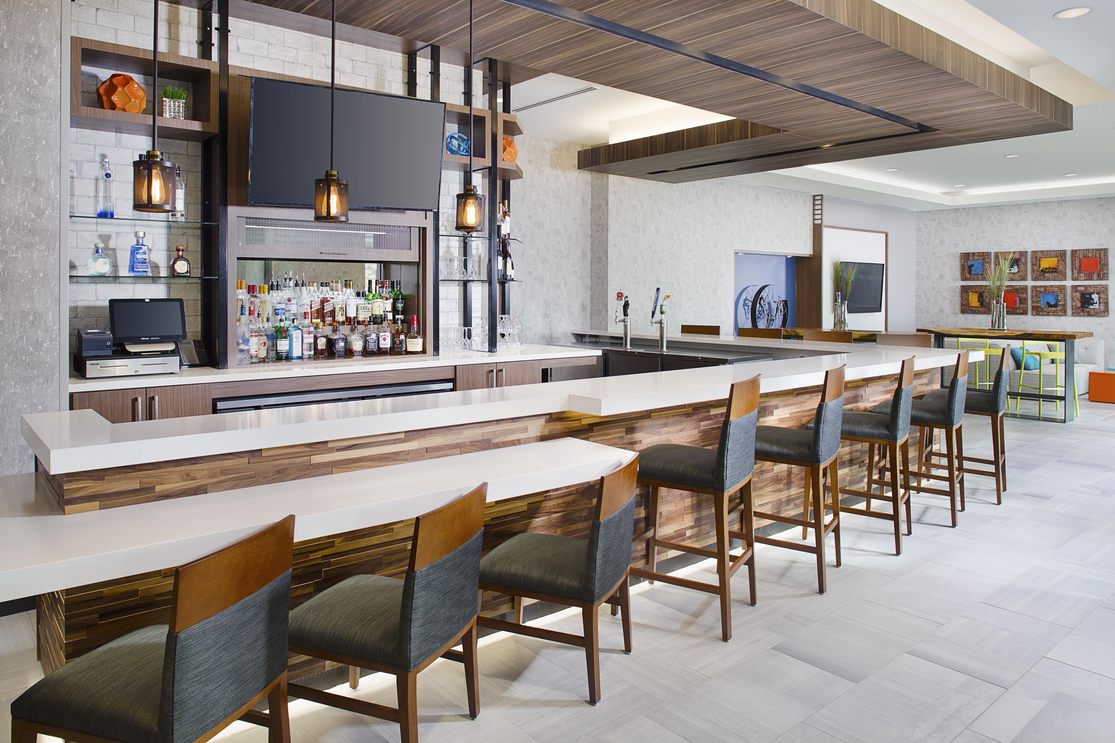 A modern bar area with a long counter, bar stools, and a variety of liquor bottles.