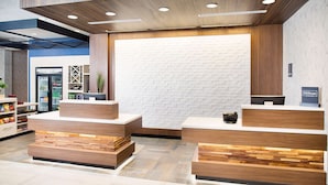 Un espace d’accueil d’hôtel au design moderne, comprenant un comptoir d’accueil, un minibar et un coin salon.