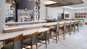 Un espace bar moderne, doté d’un long comptoir, de tabourets de bar et d’une grande variété de bouteilles.