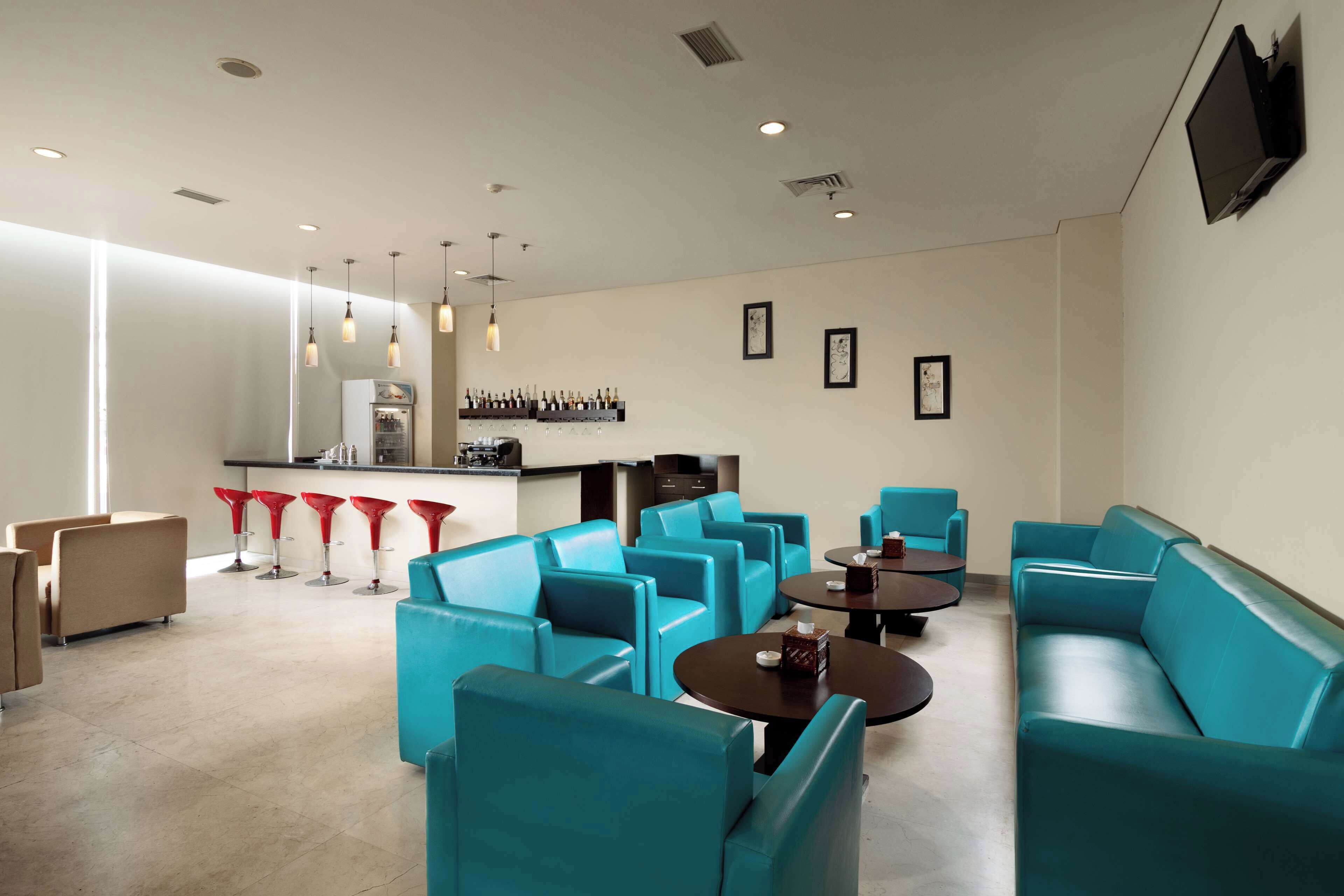 A modern lounge area with teal sofas, red bar stools, and a bar counter with wine bottles.