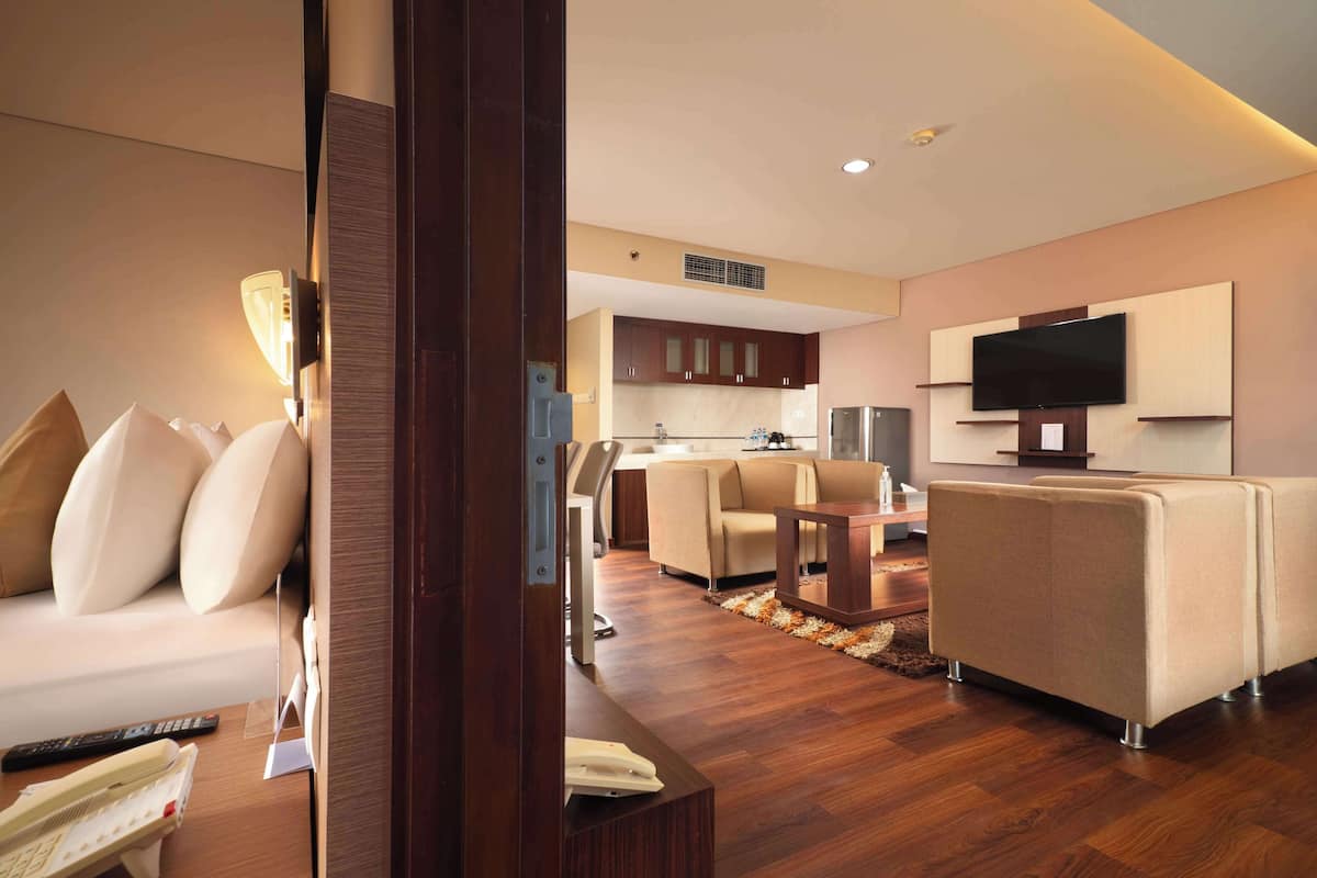 A modern hotel room with a sofa, a TV, a kitchen area, and a dining table.