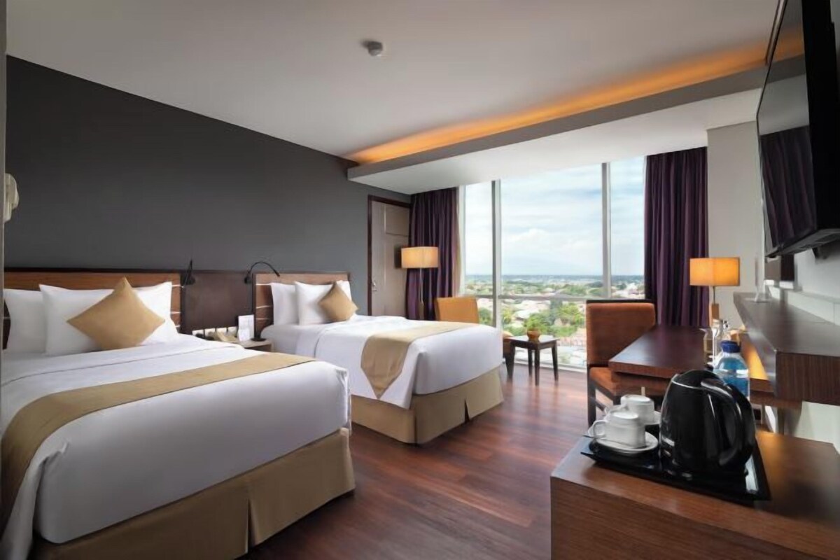 A hotel room with two beds, a desk with a coffee maker, and a view of the city.