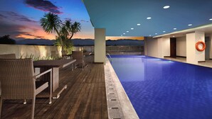 A modern indoor pool area with a wooden deck, lounge chairs, and a view of the sunset over mountains. - Best Western Plus Coco Palu (Palu)