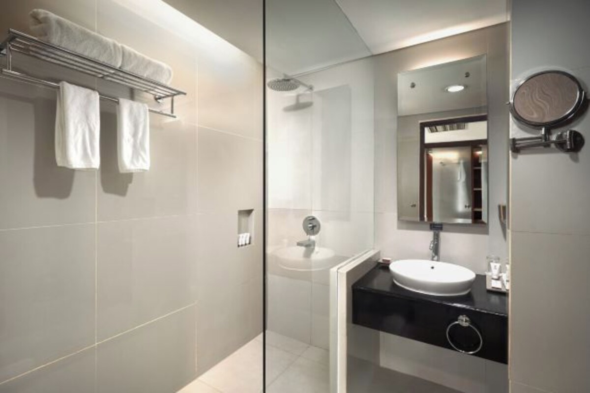 Un baño moderno con cabina de ducha de vidrio, un lavabo blanco y un perchero con dos toallas.