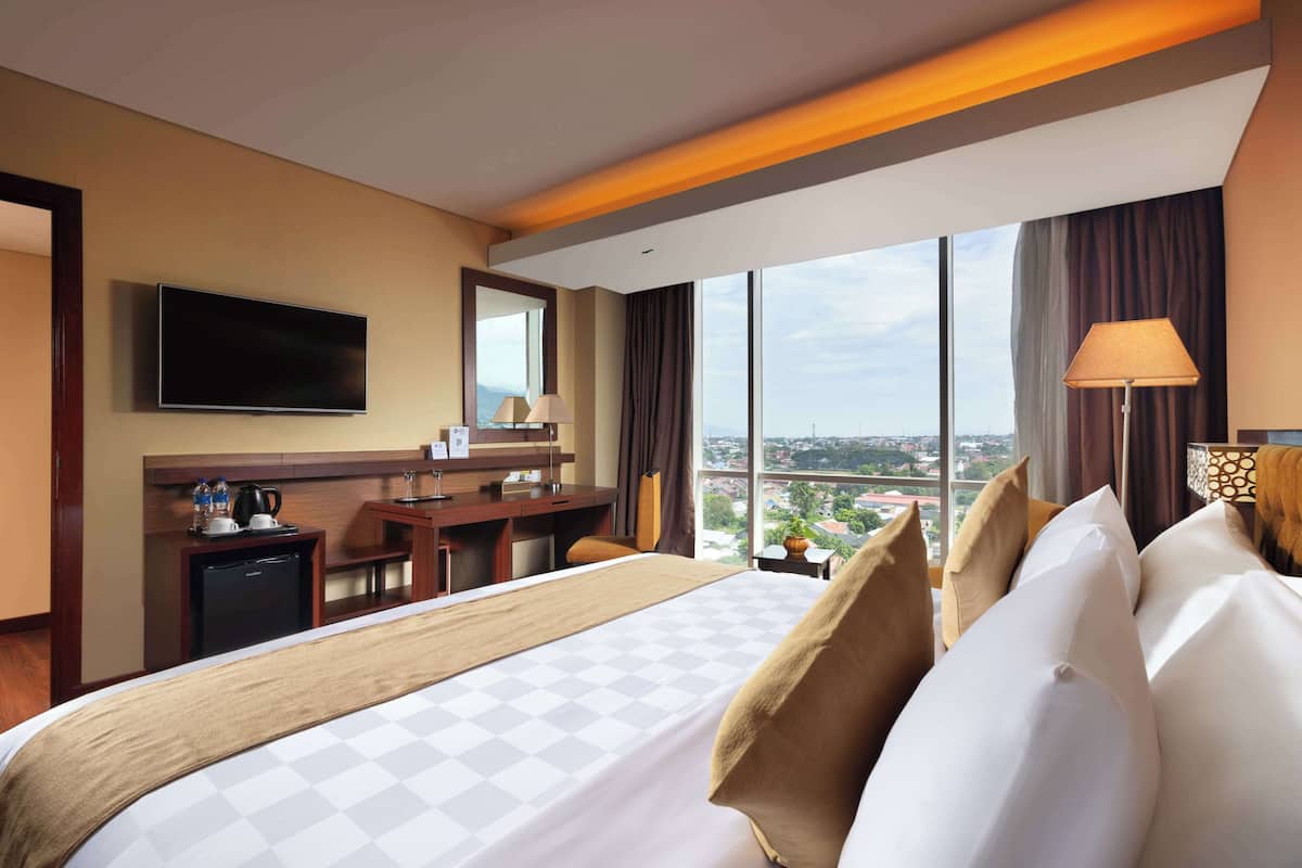 A hotel room with a large bed, a desk, a television, and a view of the city.
