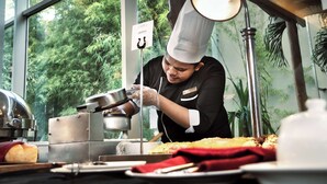 A chef preparing food in a kitchen with a view of greenery outside. - Best Western Plus Coco Palu (Palu)